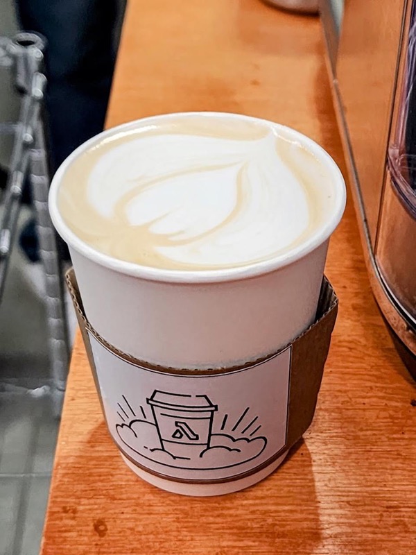 Café con arte latte en un vaso con el logo de AVIADA, sede habitual de los encuentros