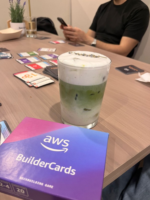 Una bebida sobre la mesa junto a la caja del juego AWS Builder Cards durante una partida